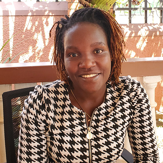 An African woman with shoulder-length brown braided hair, smiles at the camera.
