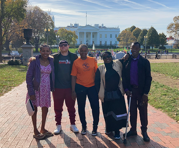 A group of five individuals, three women and two men, posing for a group photo in front of the White House in Washington DC.
