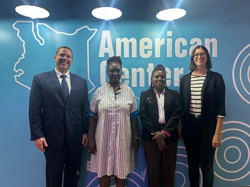 Four individuals—three women and one man—stand together for a group photo in front of a backdrop displaying a map of Kenya and the words 'American Center.'