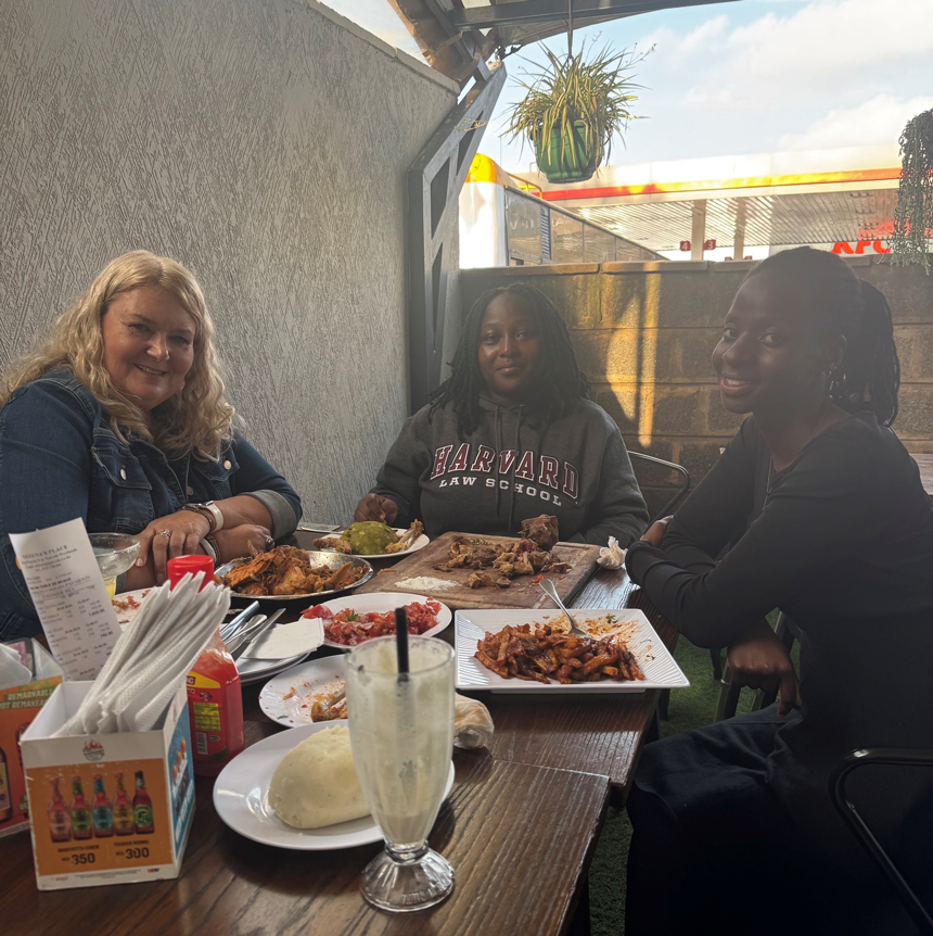 Three women are seated and smiling as they enjoy a meal.