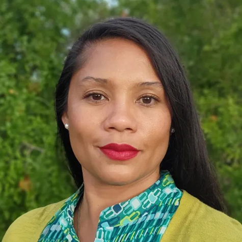 A woman with long black hair, wearing a blouse and cardigan, looking directly into the camera.