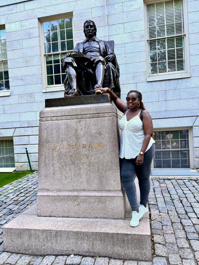 A woman stands next to a statue of a man, touching his shoe