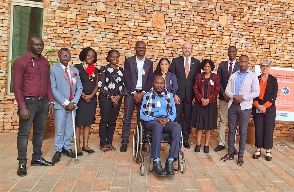 A group of 12 people, consisting of 9 Ugandans (3 women and 6 men) and 3 Americans (2 women and 1 man), posing for a group photo.