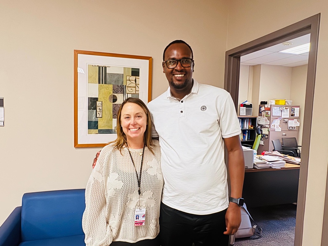 A man and a woman stand together in an office doorway, smiling at the camera.