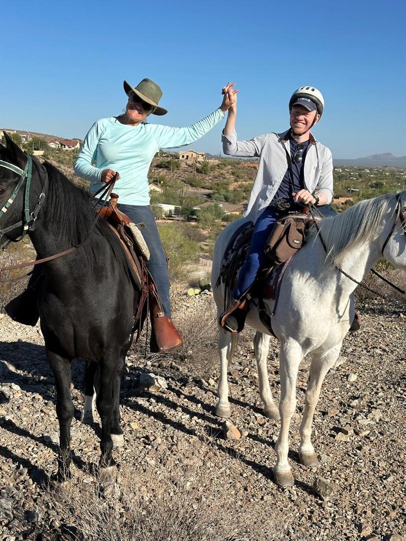 Two people riding on horseback in a desert landscape.