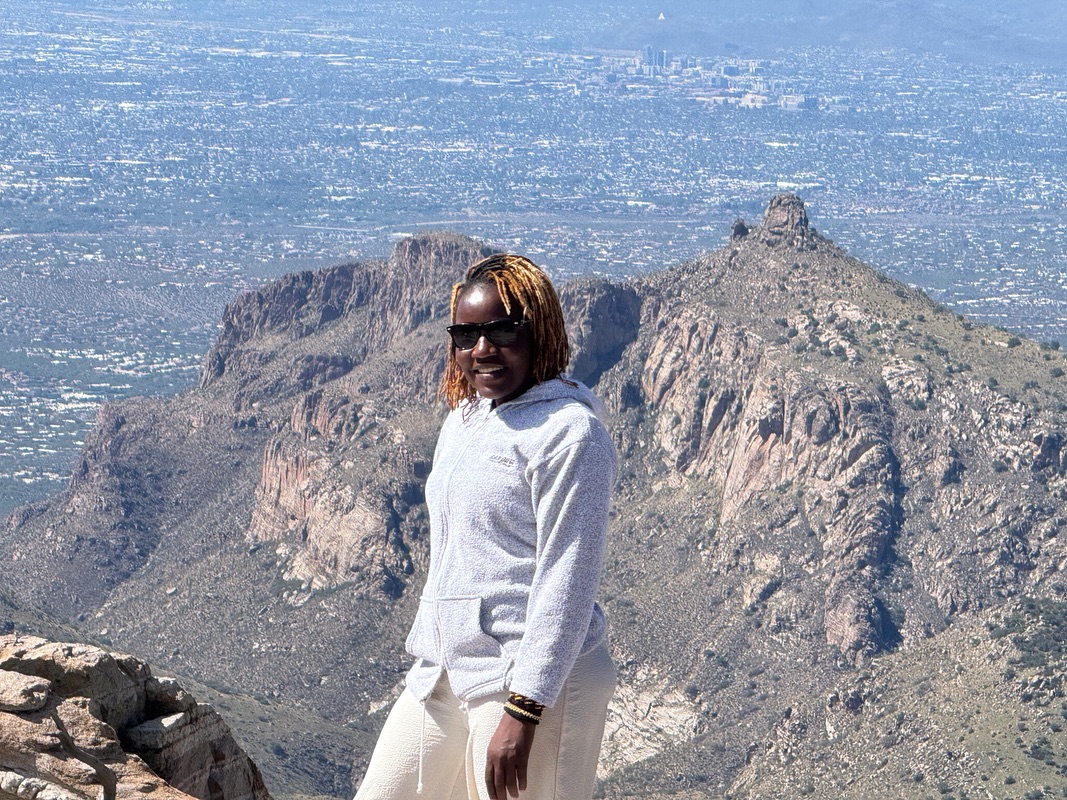 A woman standing on top of a mountain with a scenic mountainous background.