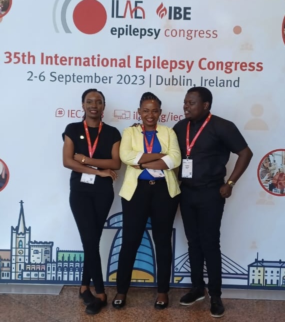 Two African women and an African man pose in front of a banner that reads 35th International Epilepsy Congress.