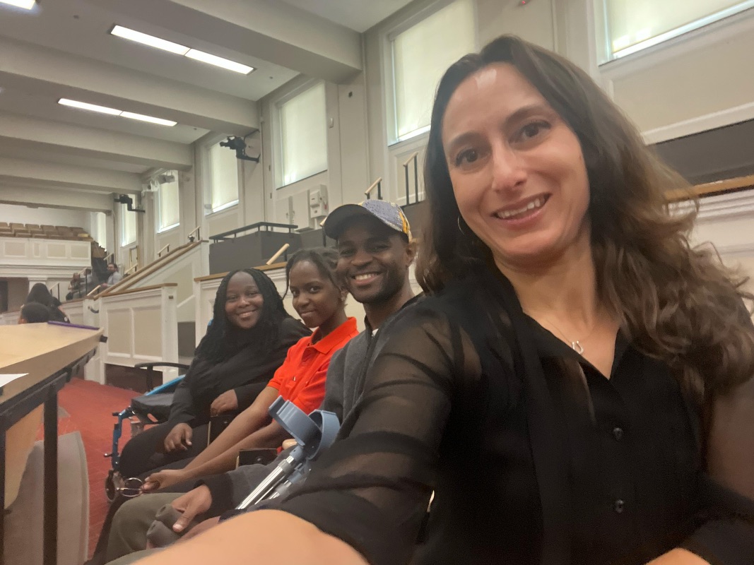 Four people seated on a bench inside an office building taking a group selfie together.