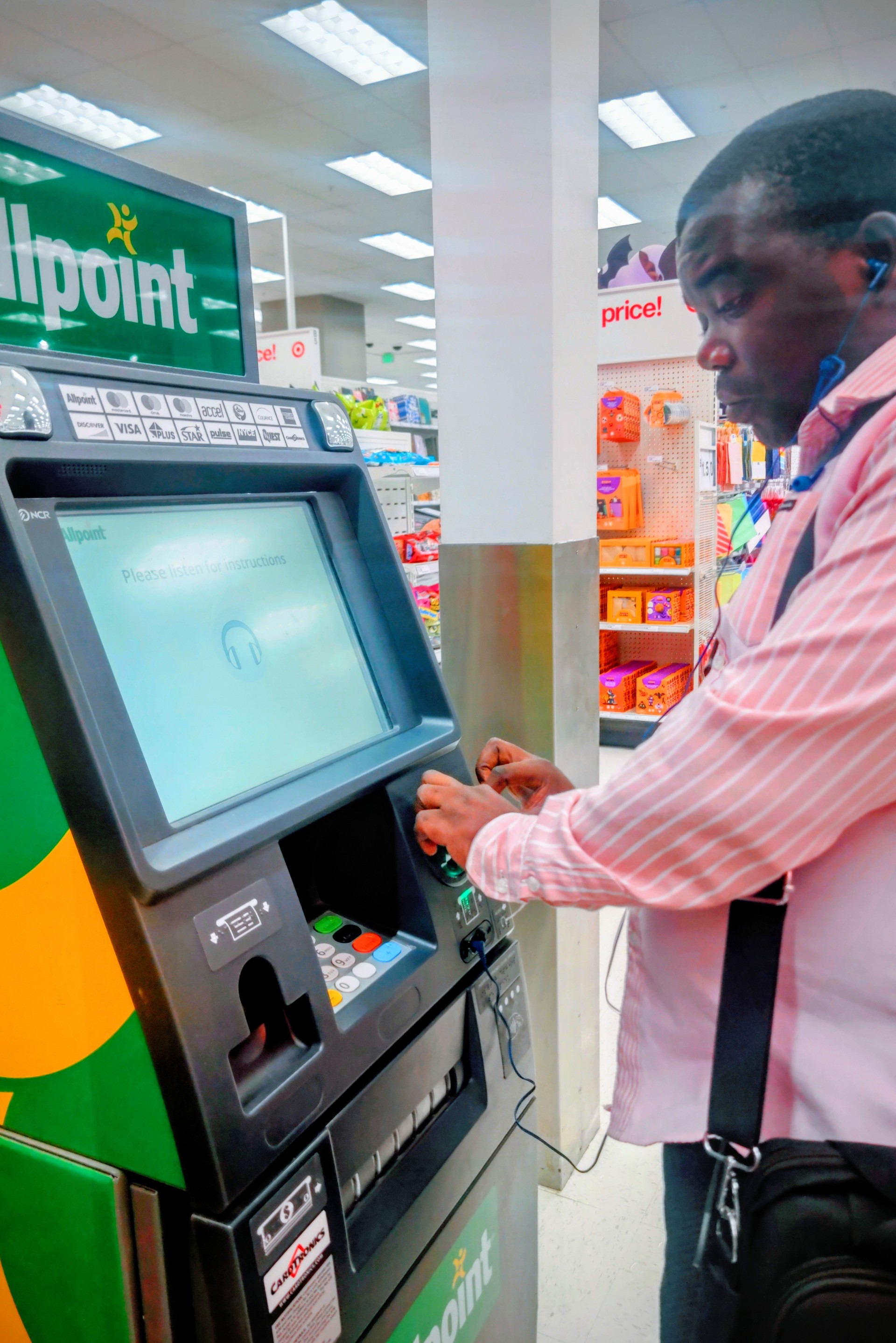 A man with earphones uses an ATM inside a supermarket.