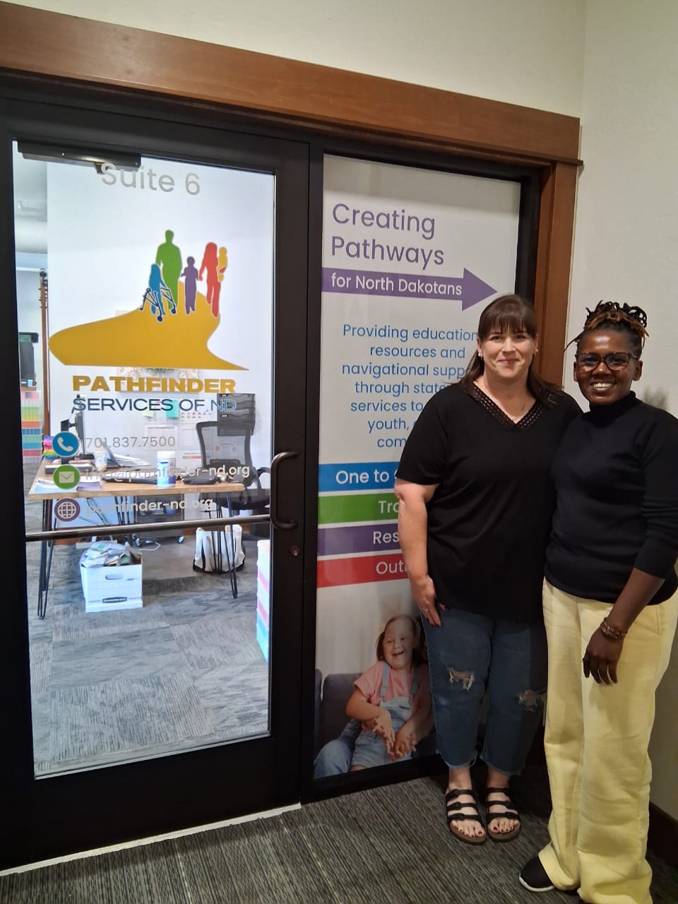 Two women stand in front of the entrance to an office.