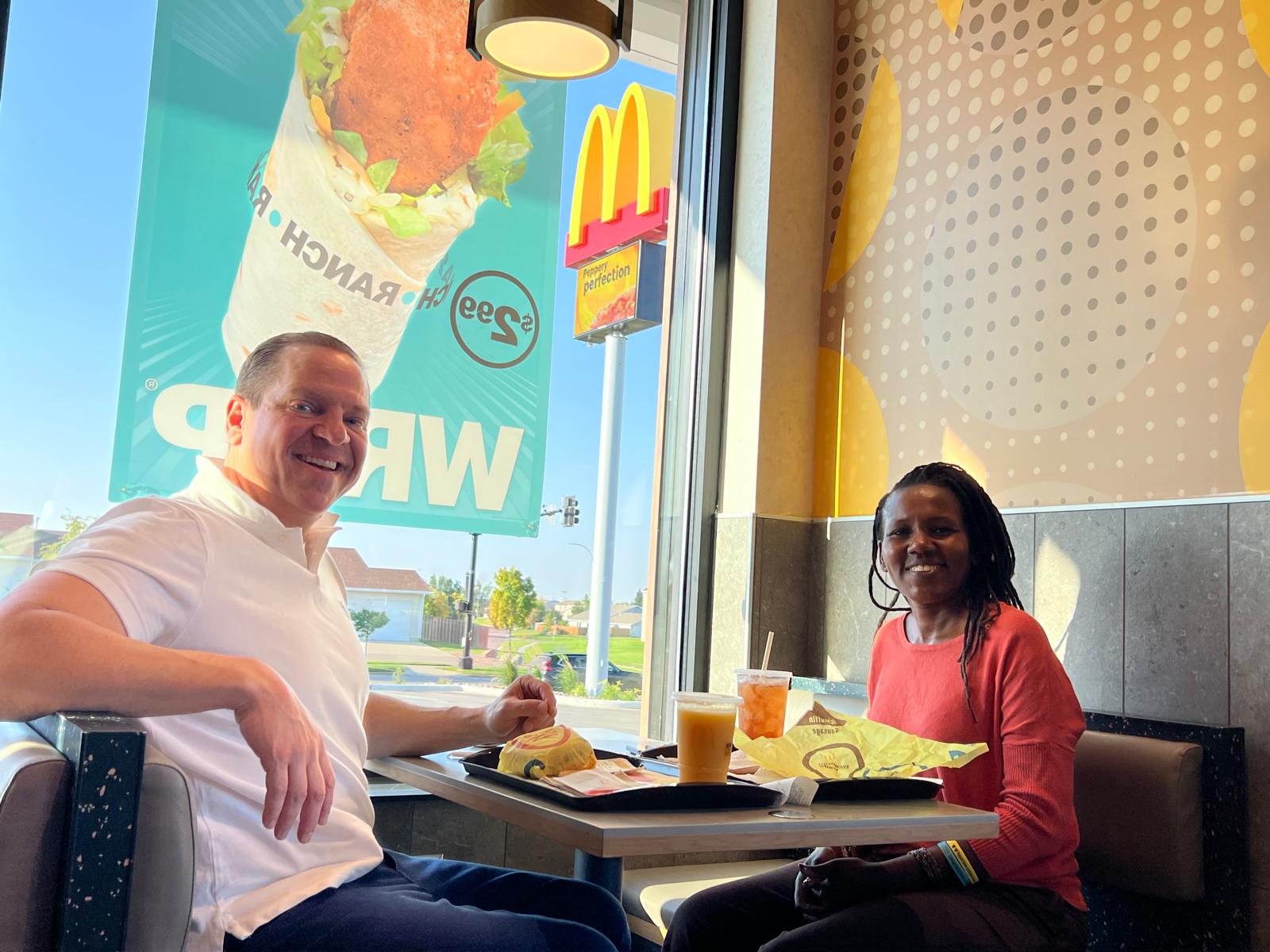 A man and a woman sit at a table in a fast-food restaurant with food and drinks on the table. 