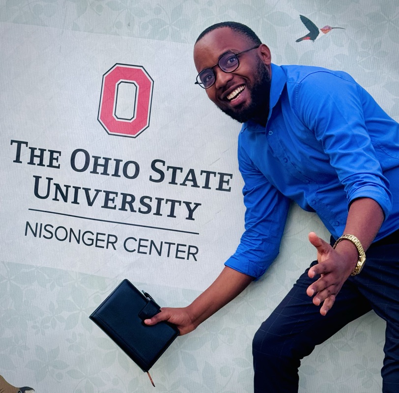  A man holding a notebook and a pen standing in front of a sign that reads “The Ohio State University – Nisonger Center.”
