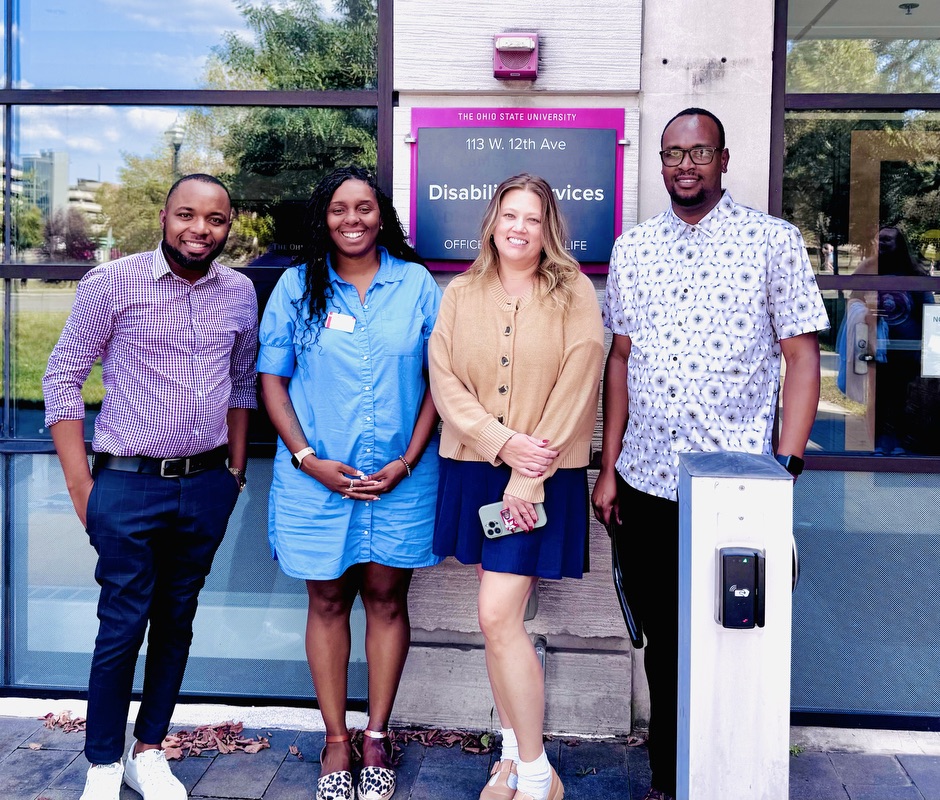 Two men and two women posing together for a photo, standing in front of an office building. 